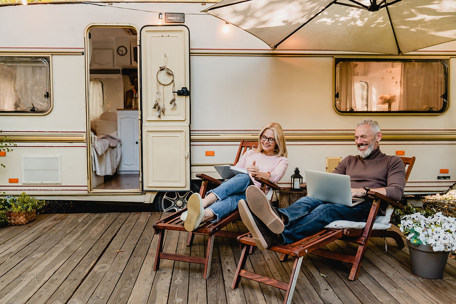 A retirement-age couple sitting on loungers on a deck outside of their mobile home, smiling and relaxing.
